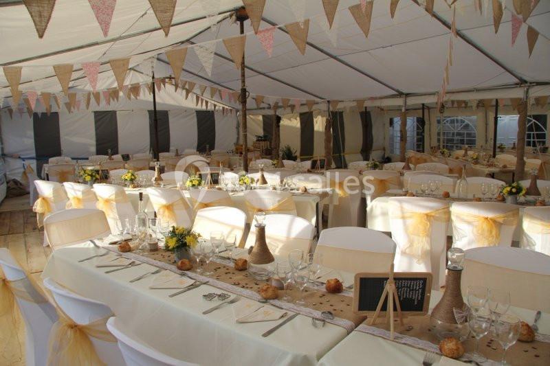 Agrandissement de la salle Salle de réception sous chapiteau décorée avec des guirlandes, des tables dressées et des chaises ornées de rubans jaunes.