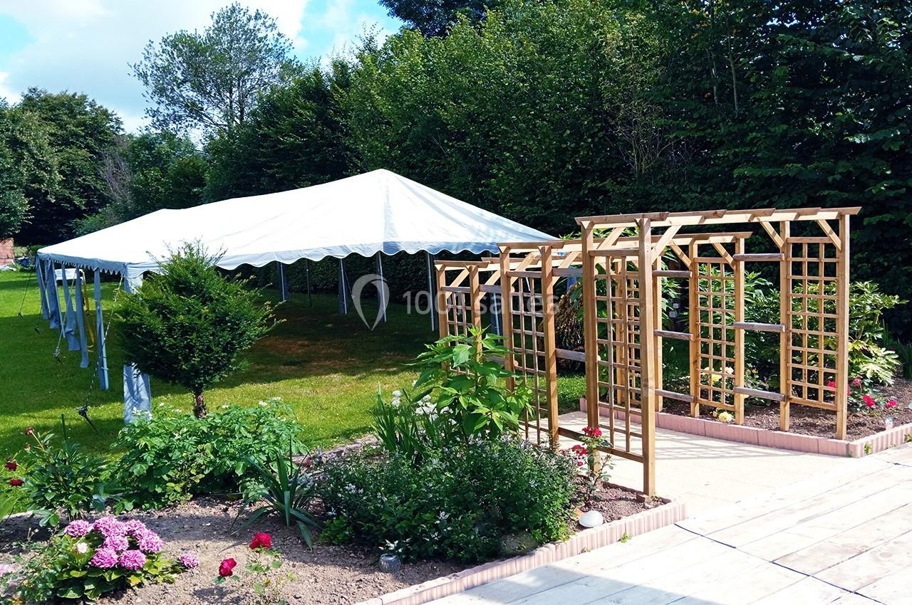 Barnum pour la cérémonie laïque Tente blanche montée sur une pelouse près d'une pergola en bois et d'un jardin fleuri, entourée de verdure.