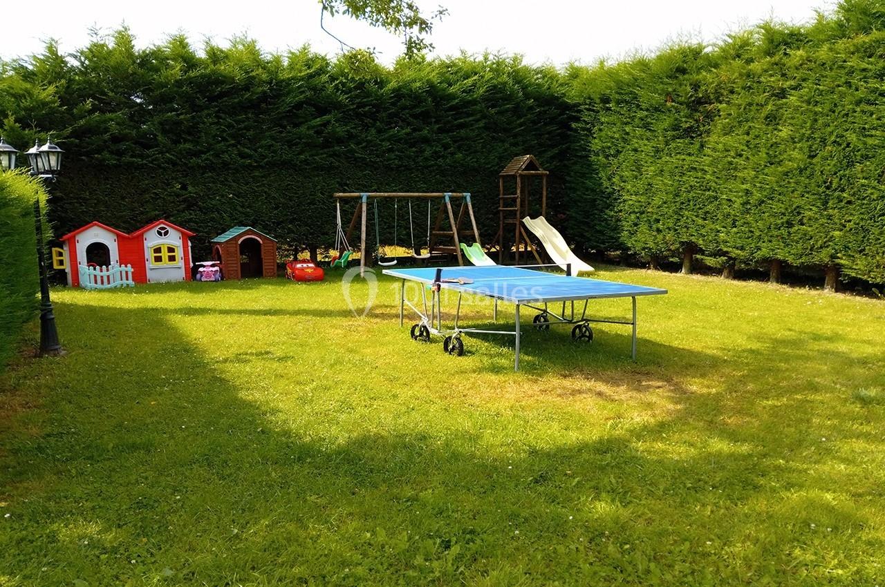 Espace de jeux Jardin avec table de ping-pong, balançoire, toboggan et petites maisons colorées entourées de haies.