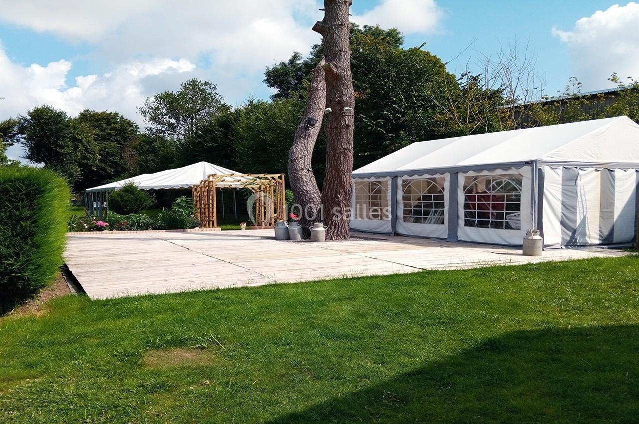 Terrasse de 110m² pour votre vin d'honneur Deux tentes blanches installées sur une terrasse en bois dans un jardin verdoyant avec arbres et ciel dégagé.