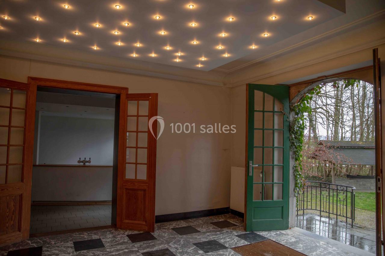Intérieur d'une pièce avec sol en marbre, portes vitrées en bois, plafond éclairé et vue sur un jardin par une porte ouverte.