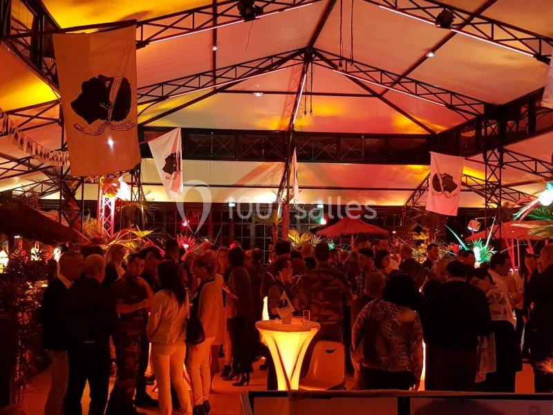 Groupe de personnes rassemblées dans un espace couvert, éclairé par des lumières rouges et décoré de drapeaux.