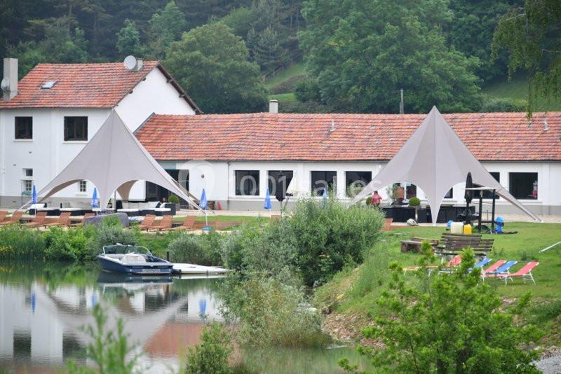 Vue d'un bâtiment blanc avec toit en tuiles rouges, entouré de tentes et d'un lac bordé de verdure.
