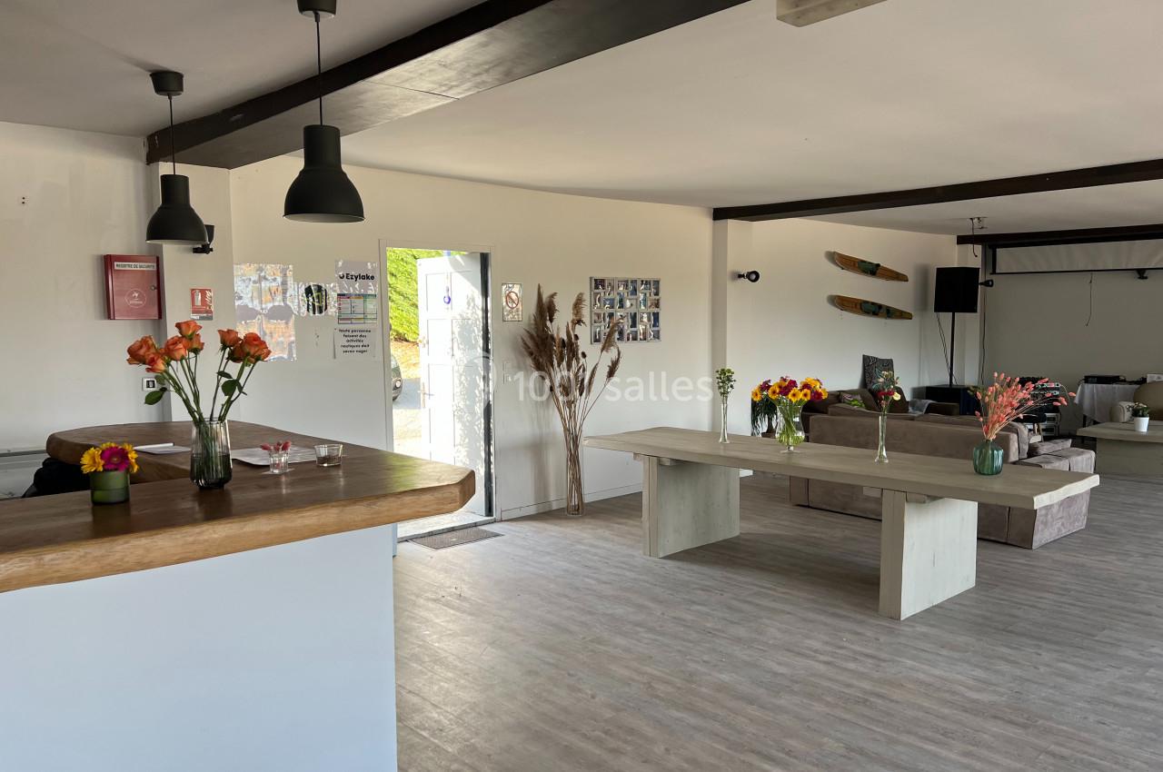 Salle lumineuse avec mobilier en bois, fleurs sur les tables, canapés au fond et décorations murales.