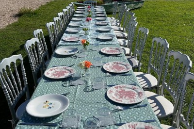 Vue d'une rivière bordée de végétation avec une maison au toit rouge et un ciel partiellement nuageux au coucher du soleil.