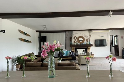 Vue d'une rivière bordée de végétation avec une maison au toit rouge et un ciel partiellement nuageux au coucher du soleil.