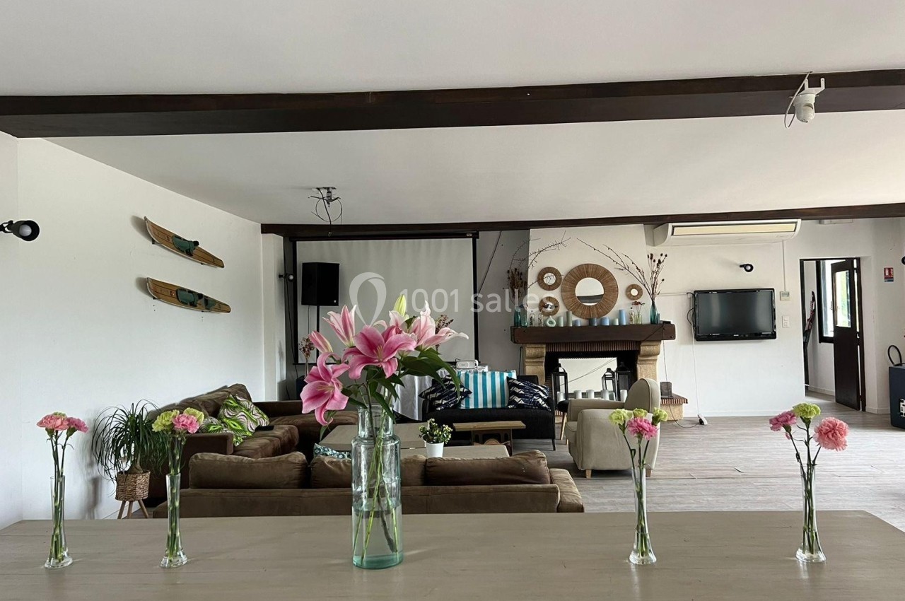 Vue d'un salon spacieux avec une décoration naturelle, des fleurs sur une table et une cheminée en arrière-plan.