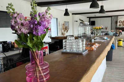 Vue d'une rivière bordée de végétation avec une maison au toit rouge et un ciel partiellement nuageux au coucher du soleil.