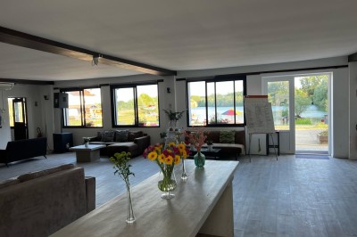 Vue d'une rivière bordée de végétation avec une maison au toit rouge et un ciel partiellement nuageux au coucher du soleil.