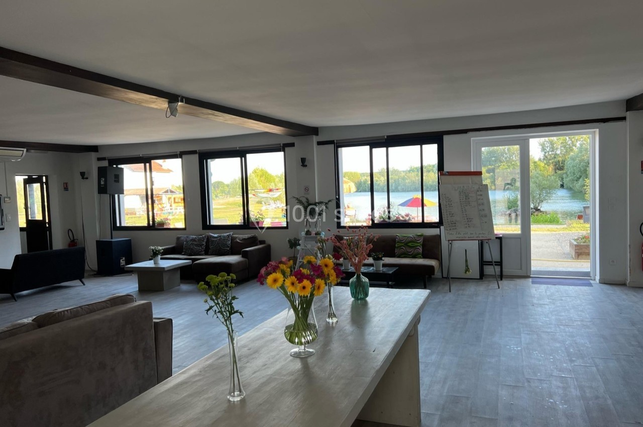 Salle lumineuse avec de grandes fenêtres, des canapés, une table ornée de fleurs et une vue sur un espace extérieur…