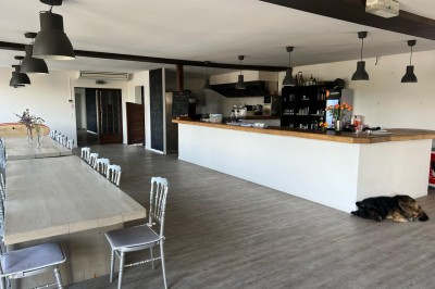 Vue d'une rivière bordée de végétation avec une maison au toit rouge et un ciel partiellement nuageux au coucher du soleil.