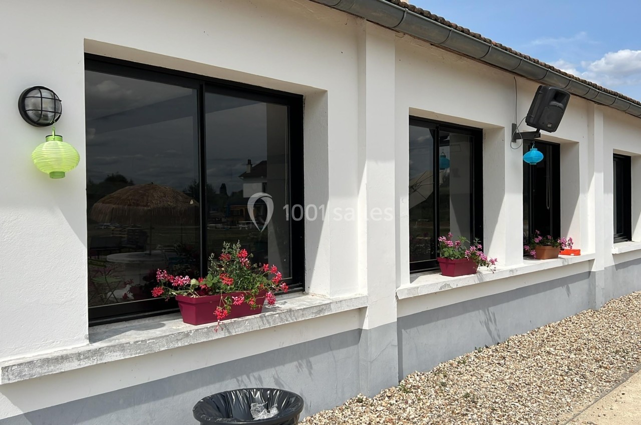 Façade blanche avec plusieurs fenêtres noires, décorées de jardinières fleuries et lanternes colorées.