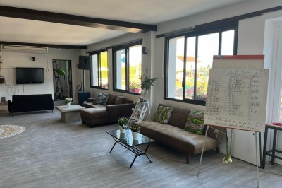 Vue d'une rivière bordée de végétation avec une maison au toit rouge et un ciel partiellement nuageux au coucher du soleil.