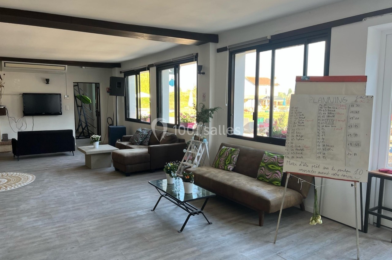 Salle lumineuse avec canapés, table basse, tableau blanc rempli d'écritures et grandes fenêtres donnant sur l'extérieur.