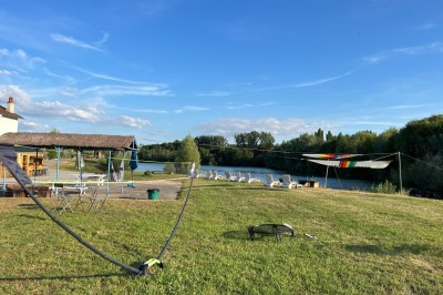 Vue d'une rivière bordée de végétation avec une maison au toit rouge et un ciel partiellement nuageux au coucher du soleil.