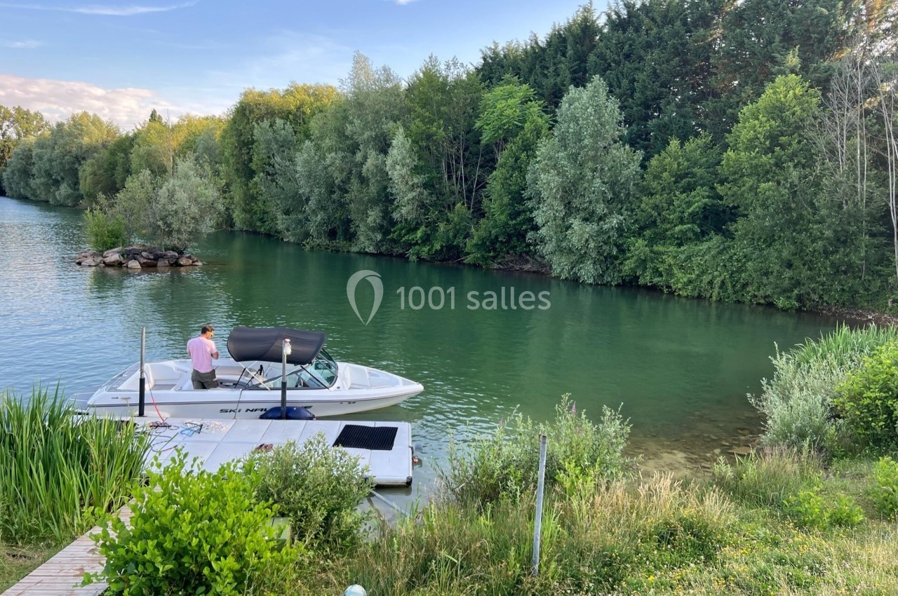 Un homme se tient sur un ponton près d'un bateau amarré sur une rivière bordée d'arbres.