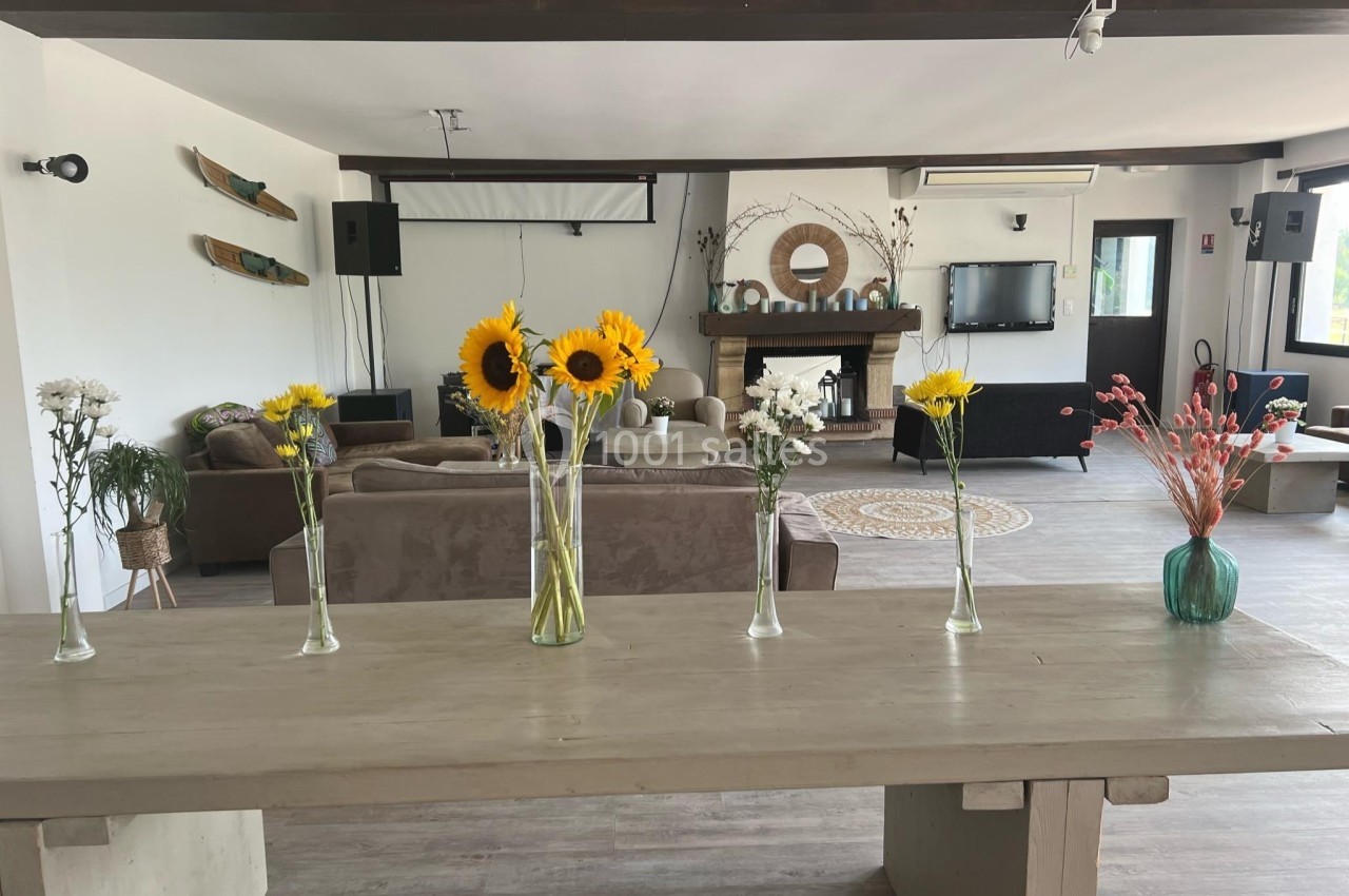 Vases avec des fleurs variées disposés sur une table en bois, dans un salon lumineux avec canapé et cheminée.