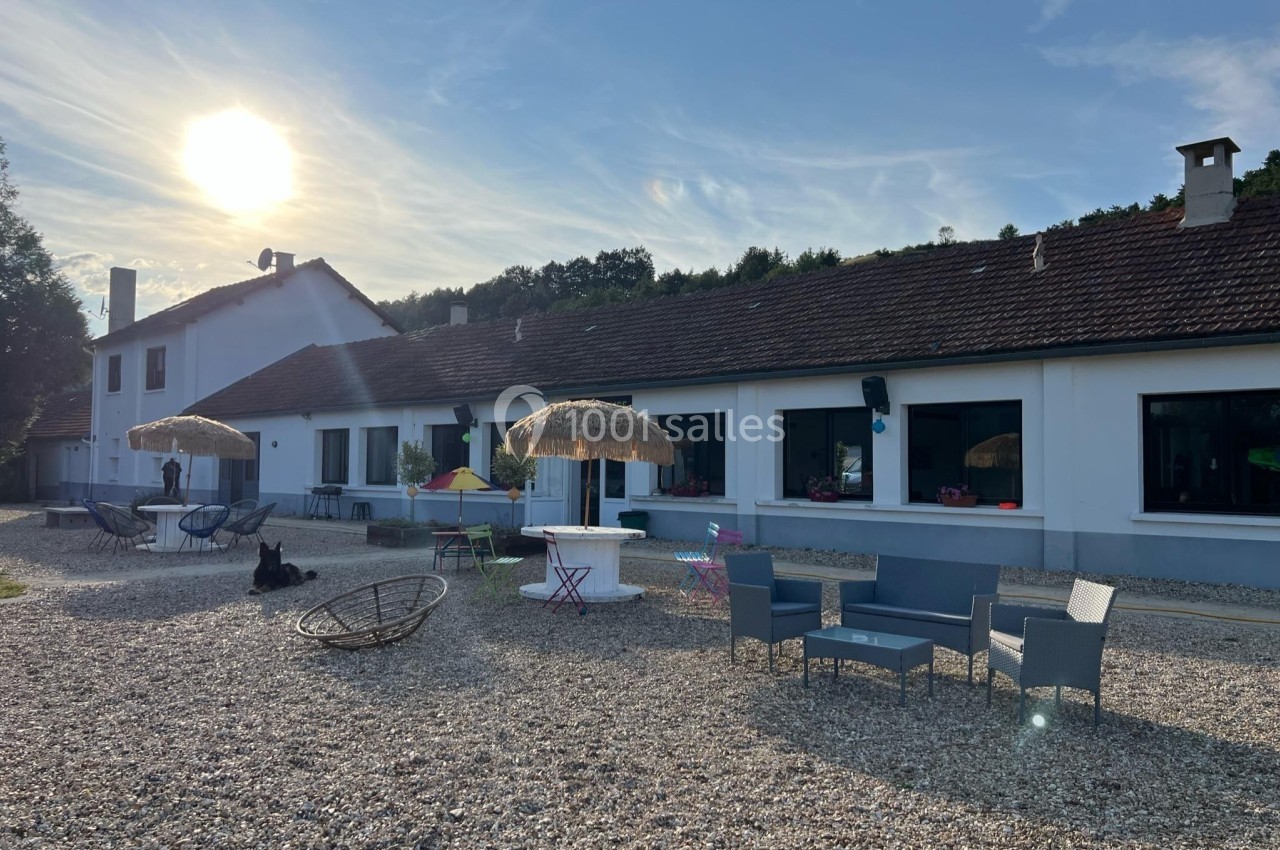 Cour extérieure d'une maison avec mobilier de jardin, parasols en paille et soleil bas dans un ciel dégagé.