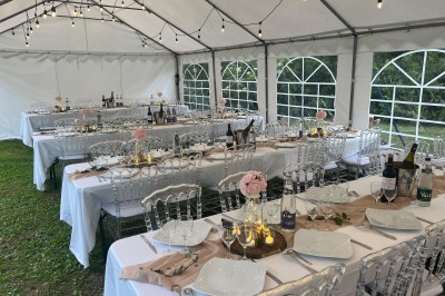 Vue d'une rivière bordée de végétation avec une maison au toit rouge et un ciel partiellement nuageux au coucher du soleil.