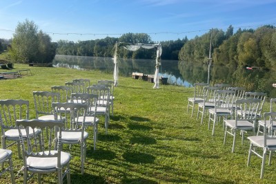 Vue d'une rivière bordée de végétation avec une maison au toit rouge et un ciel partiellement nuageux au coucher du soleil.
