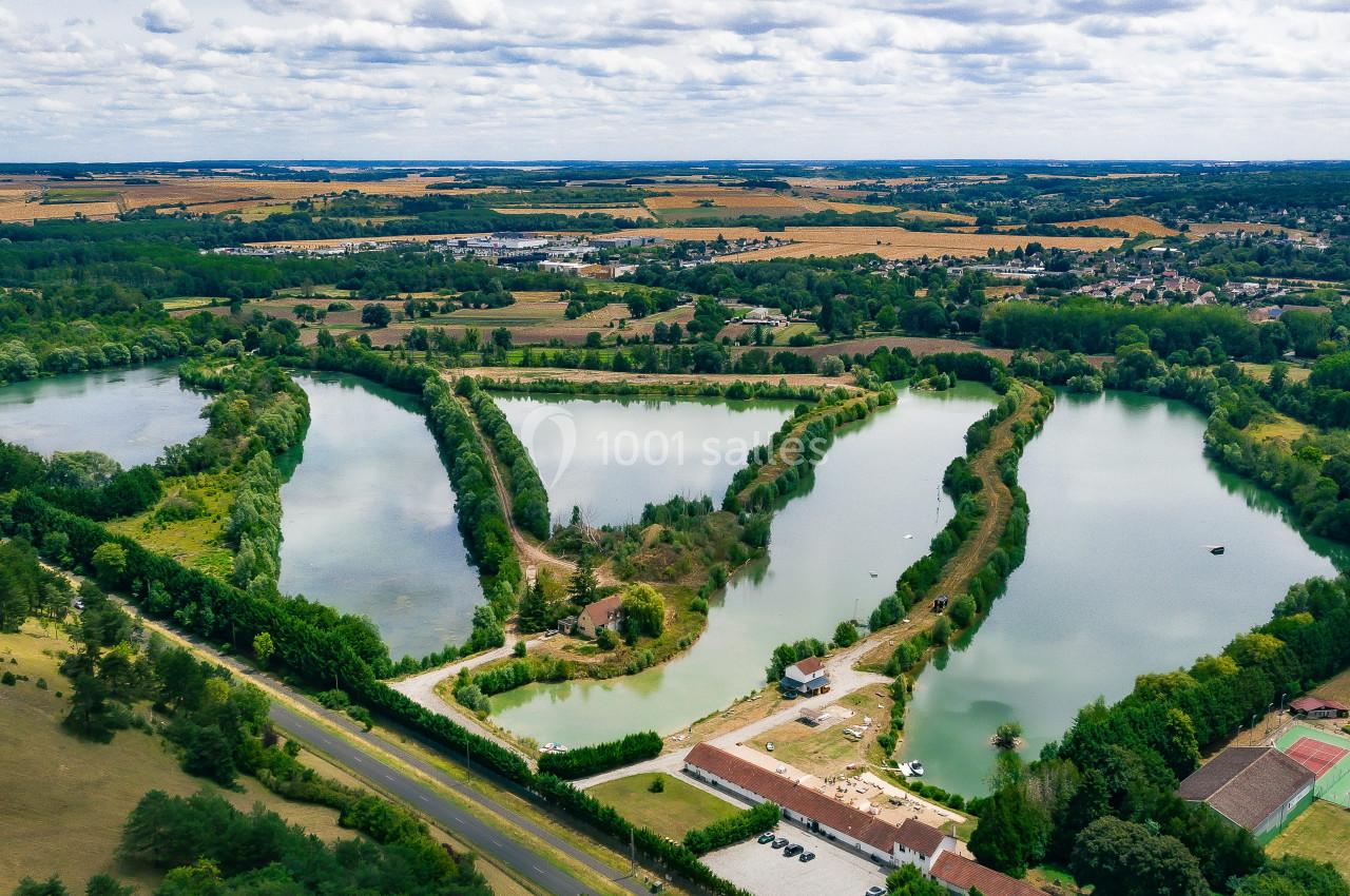 Vue aérienne de trois étangs entourés de végétation, avec des champs et des infrastructures en arrière-plan.