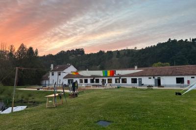 Vue d'une rivière bordée de végétation avec une maison au toit rouge et un ciel partiellement nuageux au coucher du soleil.