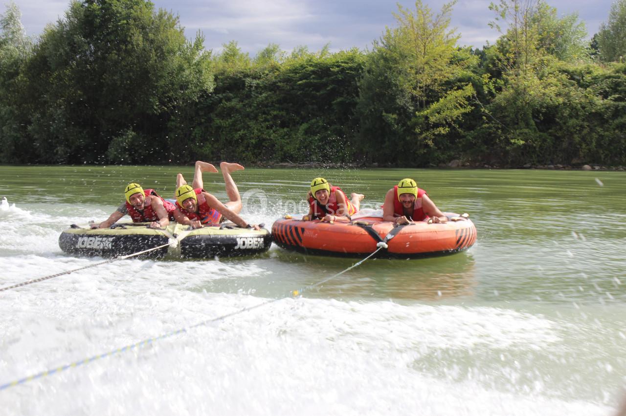 Des personnes portant des gilets de sauvetage s'accrochent à des bouées tractées sur une rivière entourée de végétation.