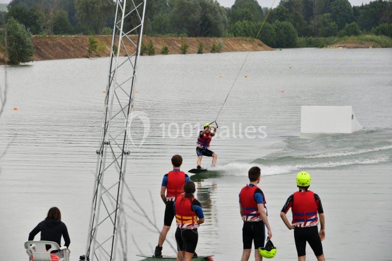 Un groupe de personnes en gilets de sauvetage observe un wakeboarder tracté sur un lac.