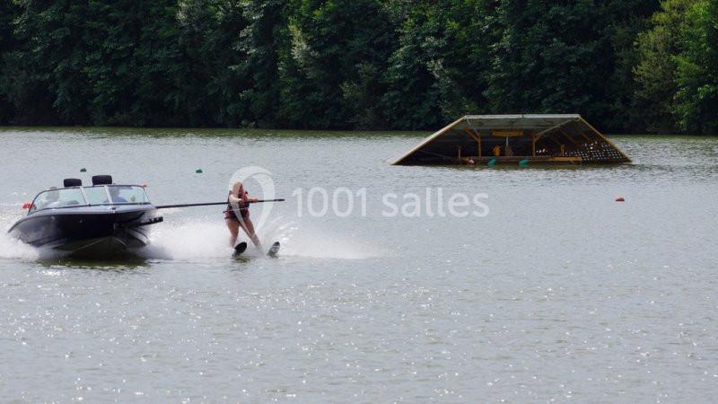 Une personne fait du ski nautique tractée par un bateau sur un lac entouré de végétation.