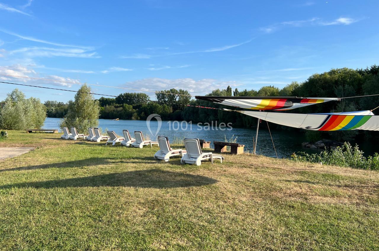 Chaises longues alignées sur une pelouse au bord d'une rivière, avec un grand auvent coloré tendu au-dessus.