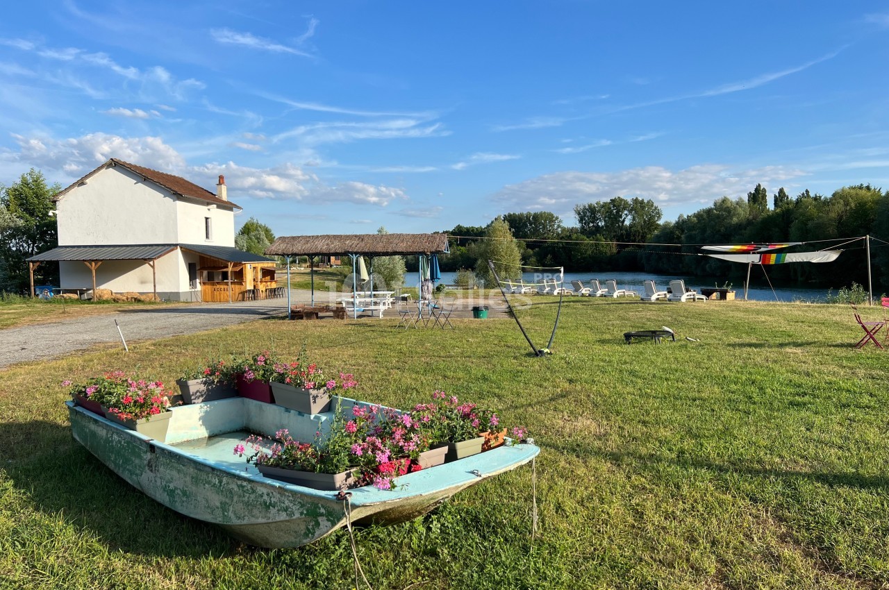 Barque fleurie sur une pelouse près d'une maison blanche, avec des tables, un auvent et une rivière en arrière-plan.