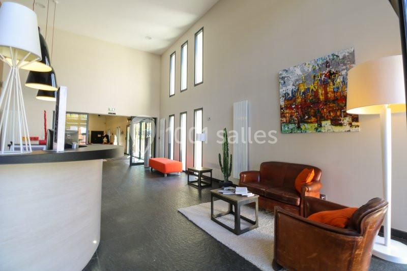 Hall d'entrée lumineux avec canapé en cuir, fauteuil, tables basses, lampes et tableau coloré au mur.