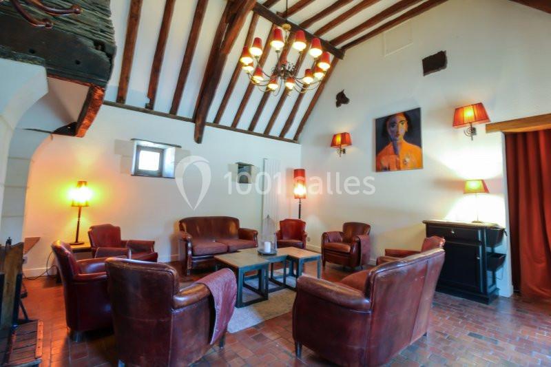 Salon chaleureux avec poutres apparentes, fauteuils en cuir, éclairage tamisé et tableau coloré sur le mur.
