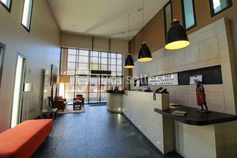 Réception moderne avec comptoir en bois, luminaires suspendus noirs et espace d'attente avec canapé orange.