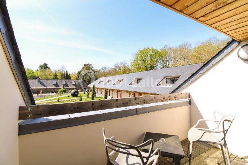 Vue depuis un balcon avec table et chaises, donnant sur des bâtiments à toits en ardoise entourés de verdure.