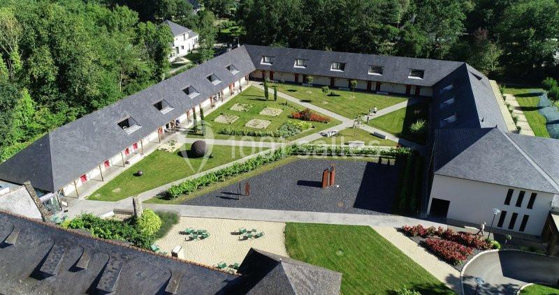 Vue aérienne d'un bâtiment en U entourant une cour paysagée avec pelouses, allées et sculptures modernes.