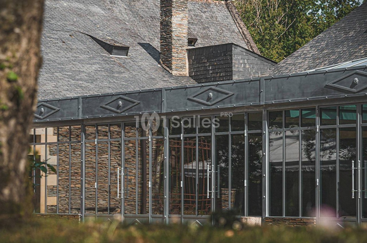 Façade vitrée d'un bâtiment moderne avec toit en ardoise, entouré de verdure.
