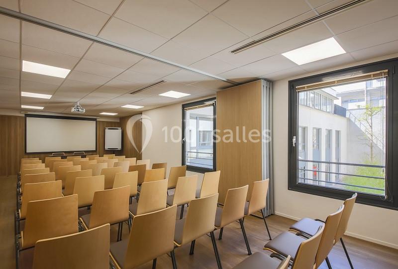 Salle de conférence lumineuse avec rangées de chaises en bois, un écran de projection et des fenêtres donnant sur l…