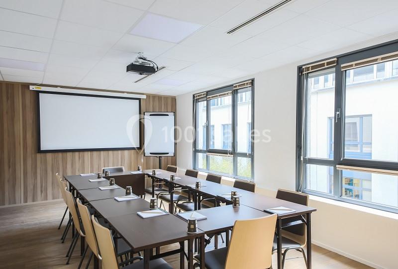 Salle de réunion lumineuse avec une grande table, des chaises, un tableau blanc et un écran de projection.