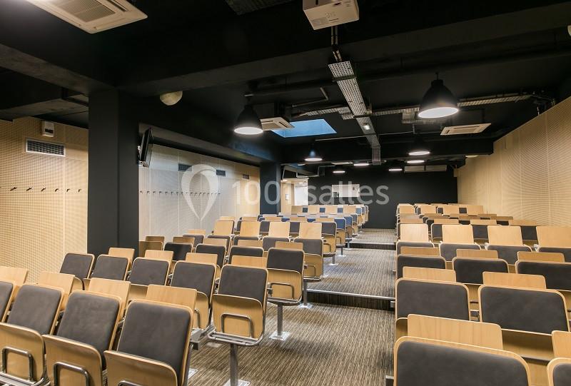Salle de conférence moderne avec rangées de sièges en bois et éclairage suspendu.