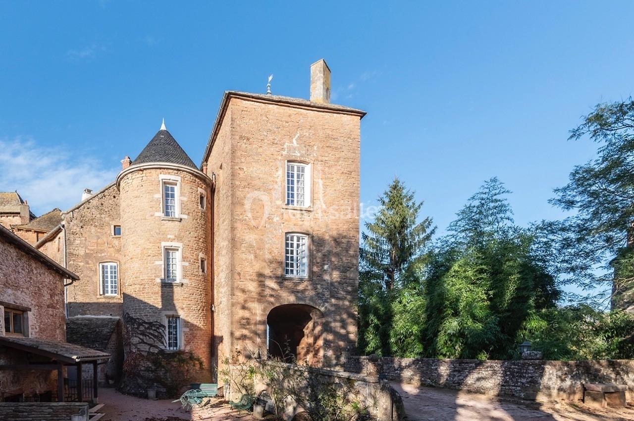 Façade d'un château en pierre rouge avec tours et fenêtres, entouré de végétation sous un ciel bleu.