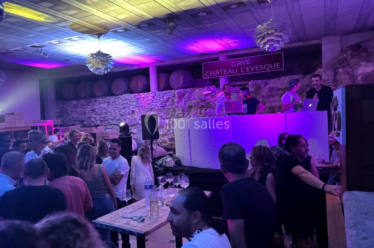 Soirée dans une cave avec DJ sur scène, invités dansant ou discutant sous un éclairage coloré.