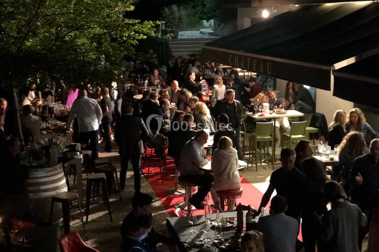 Terrasse animée en soirée avec des tables occupées par des convives, éclairage tamisé et ambiance conviviale.