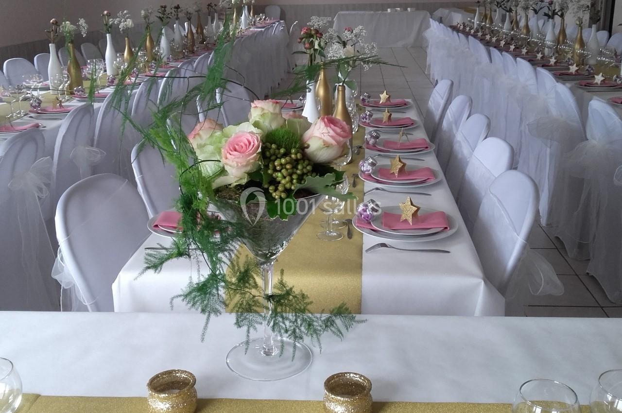 Salle de réception décorée avec des tables alignées, nappes blanches, chemins de table dorés et centre de table floral.