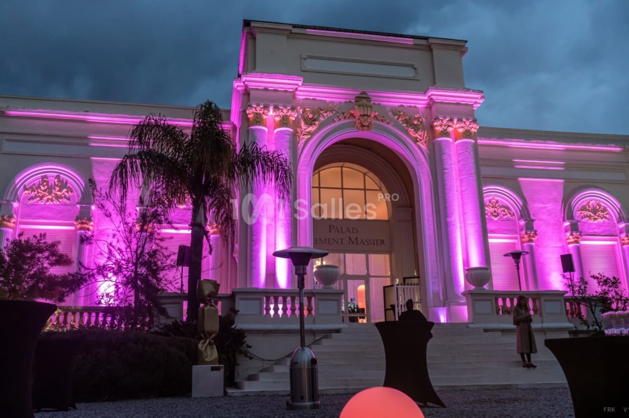 Façade d'un bâtiment éclairé en rose avec des colonnes et une grande arche, vue de nuit avec un ciel nuageux.