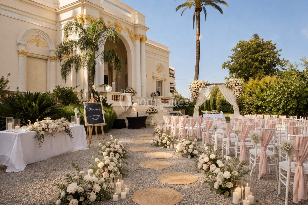 Allée décorée de fleurs menant à une cérémonie de mariage en plein air devant un bâtiment élégant.