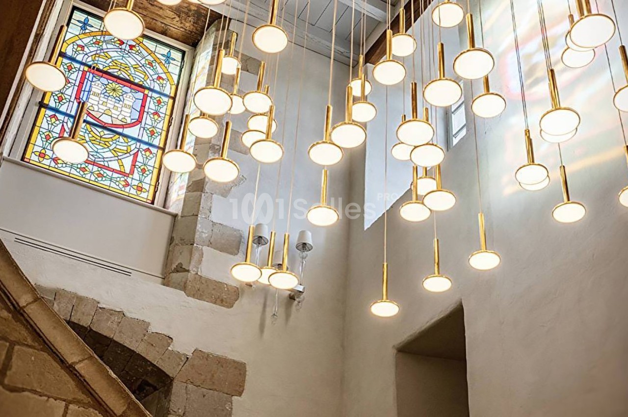 Suspension lumineuse moderne avec de multiples ampoules rondes dans un intérieur avec vitrail coloré et murs en pierre.
