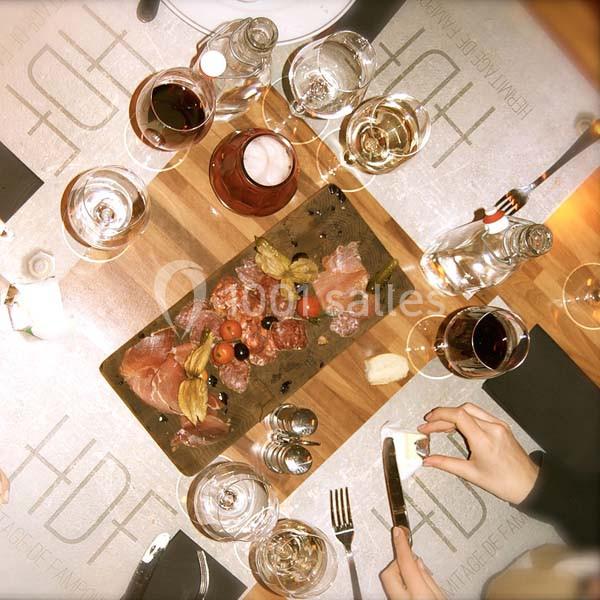 Plateau de charcuterie avec tomates cerises et physalis, entouré de verres de vin et couverts sur une table dressée.