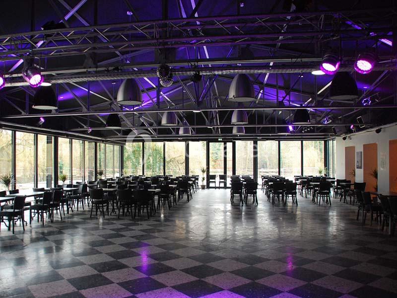 Salle spacieuse avec des tables et des chaises, éclairée par des lumières violettes et dotée de grandes baies vitrées…