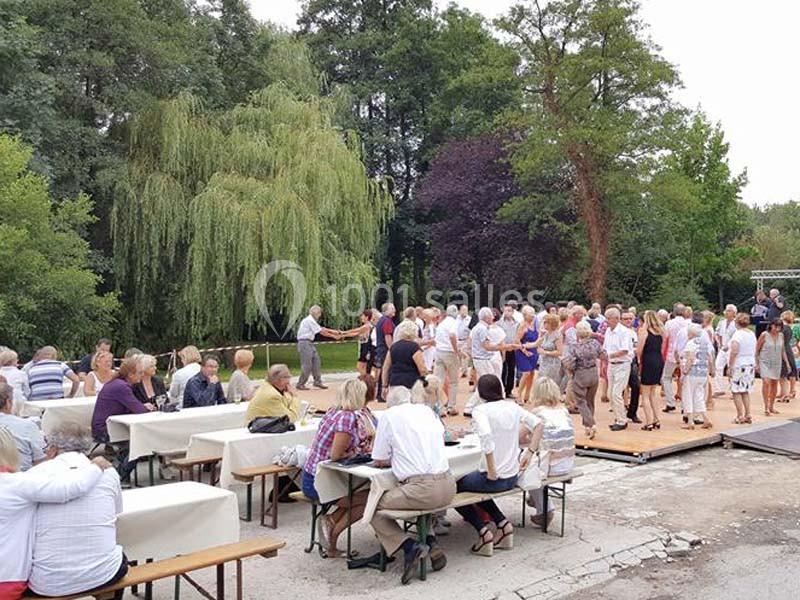 Des personnes dansent et discutent sur une piste en plein air, entourées de tables et d'arbres verdoyants.